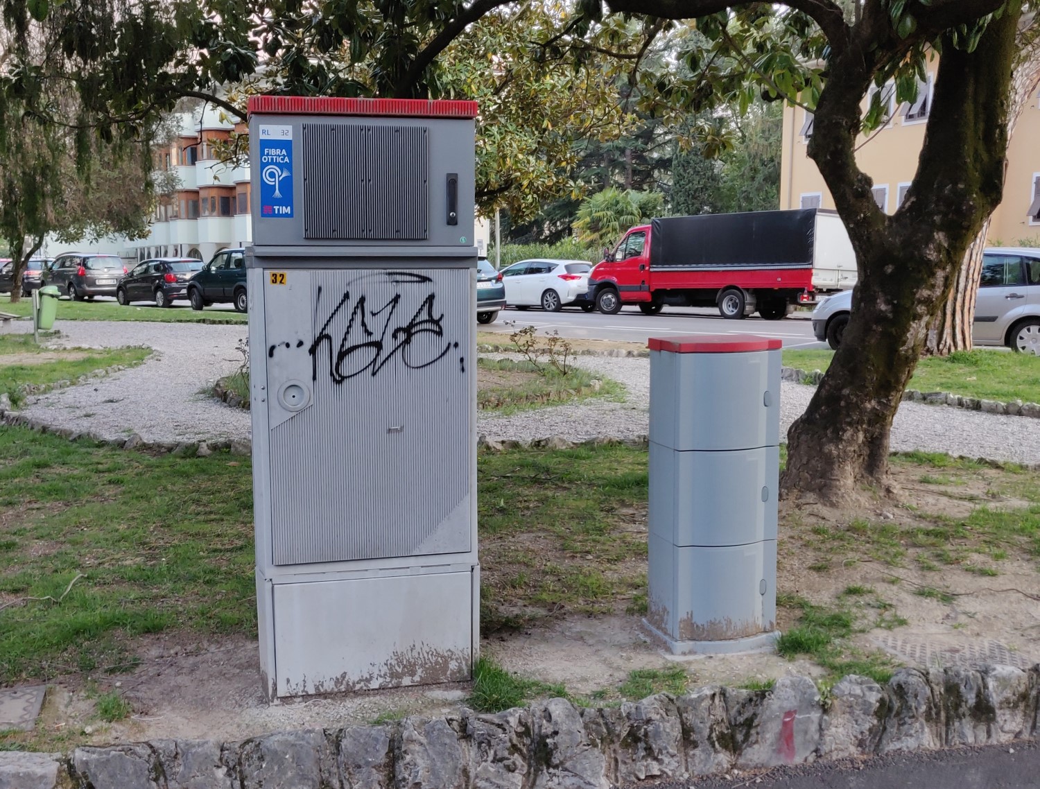 A sinistra, un armadio ripartilinea TIM con sopra una scatola con il tetto rosso, a destra, una colonnina stretta e alta con il tetto rosso.